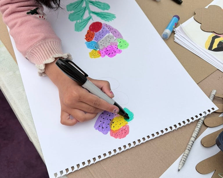 Child drawing a colorful rainbow flower on a notebook with markers.